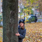 Девушка в сером пальто выглядывает из-за дерева в осеннем парке - Украина, Одесса, 09,11,2019