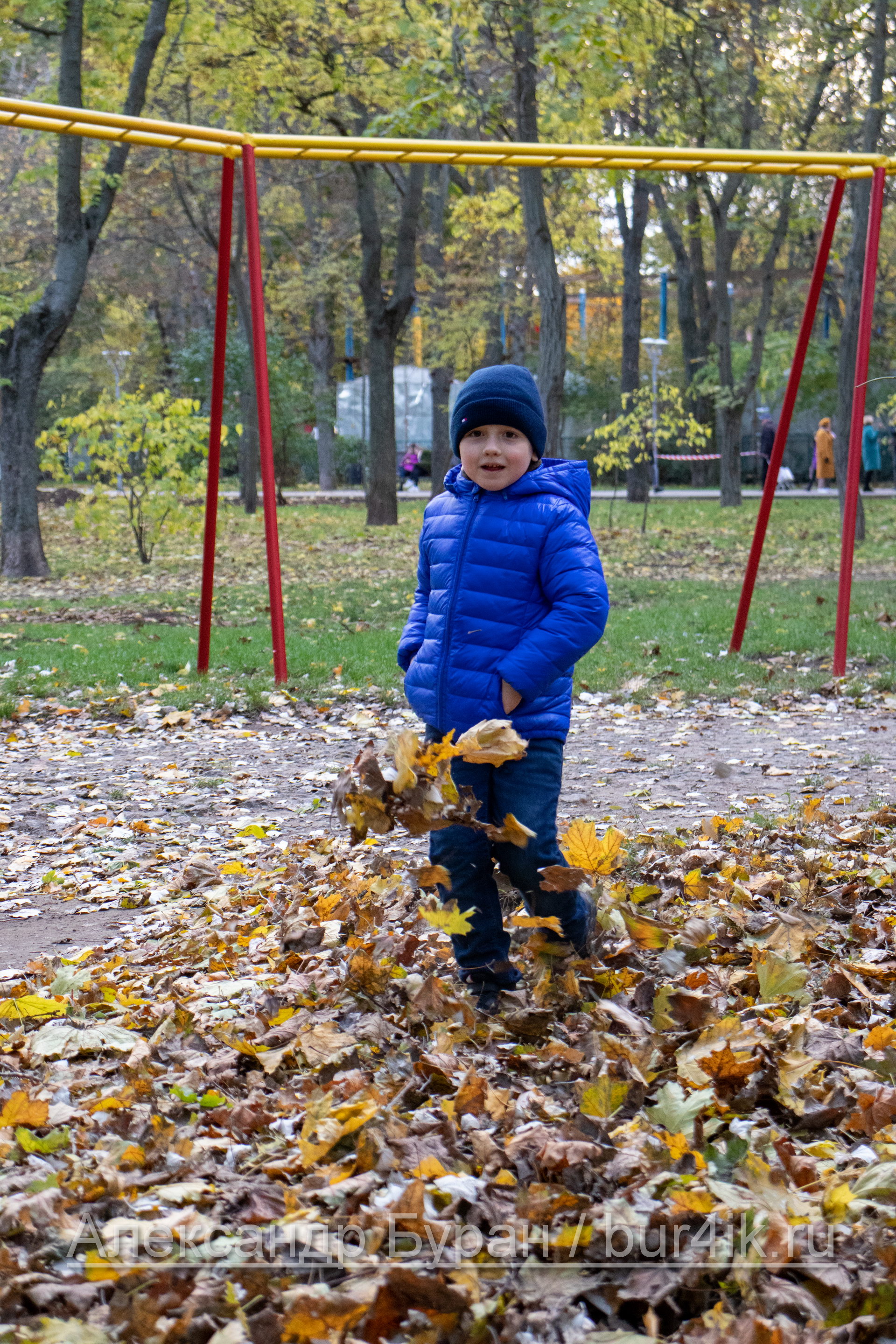 Мальчик в осеннем парке подбрасывает листья с ноги