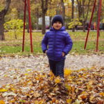 Мальчик стоит в осеннем парке среди опавших желтых листьев