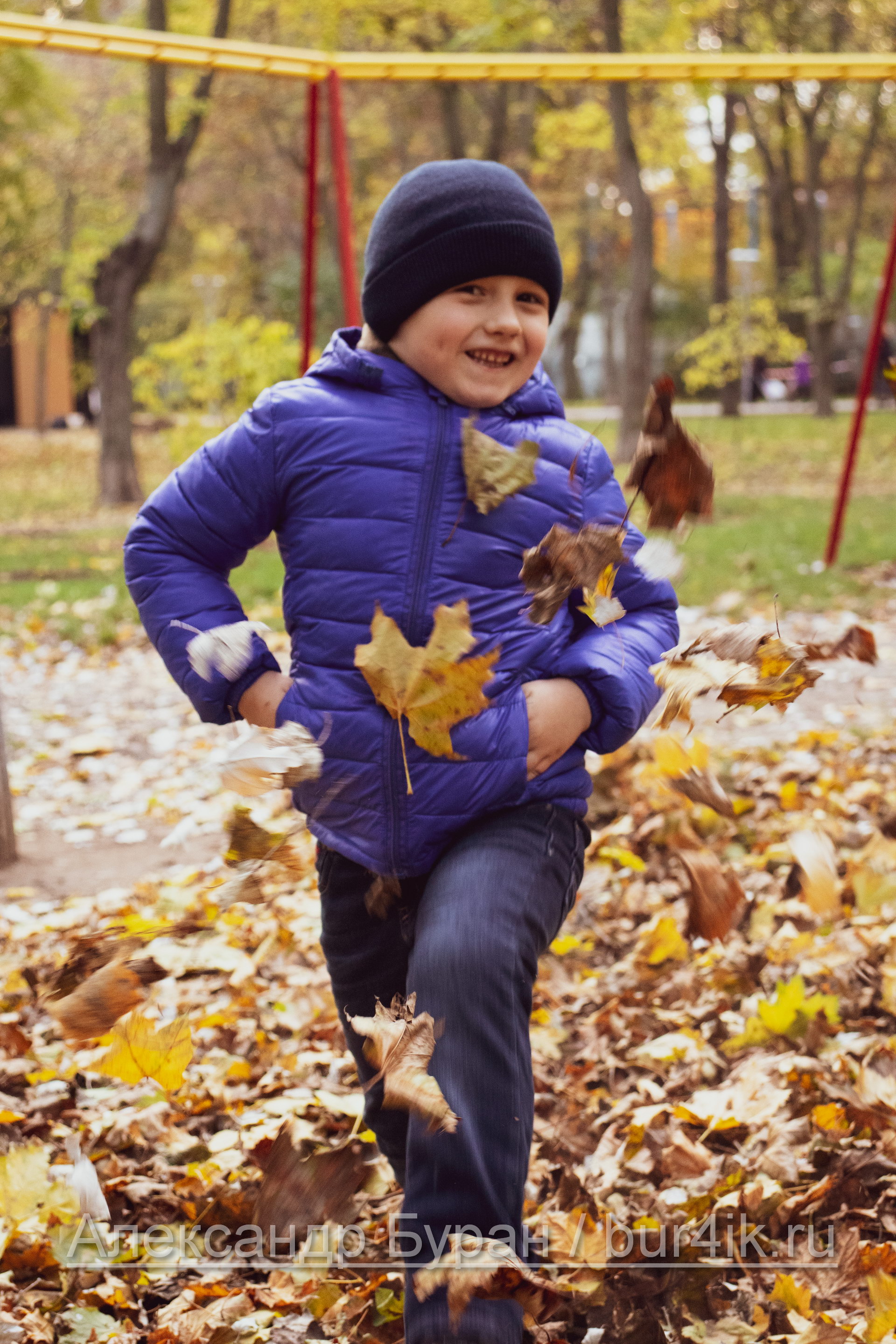 Мальчик играет в синей куртке с листьями в осеннем парке