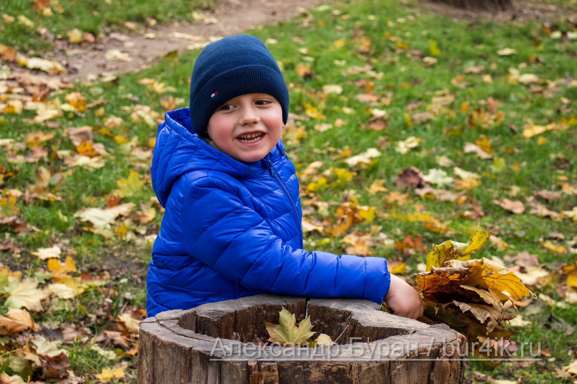 Мальчик играет в синей фуражке с листьями в осеннем парке