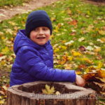 Мальчик в светло-синем пиджаке сидит на пеньке в парке осенью