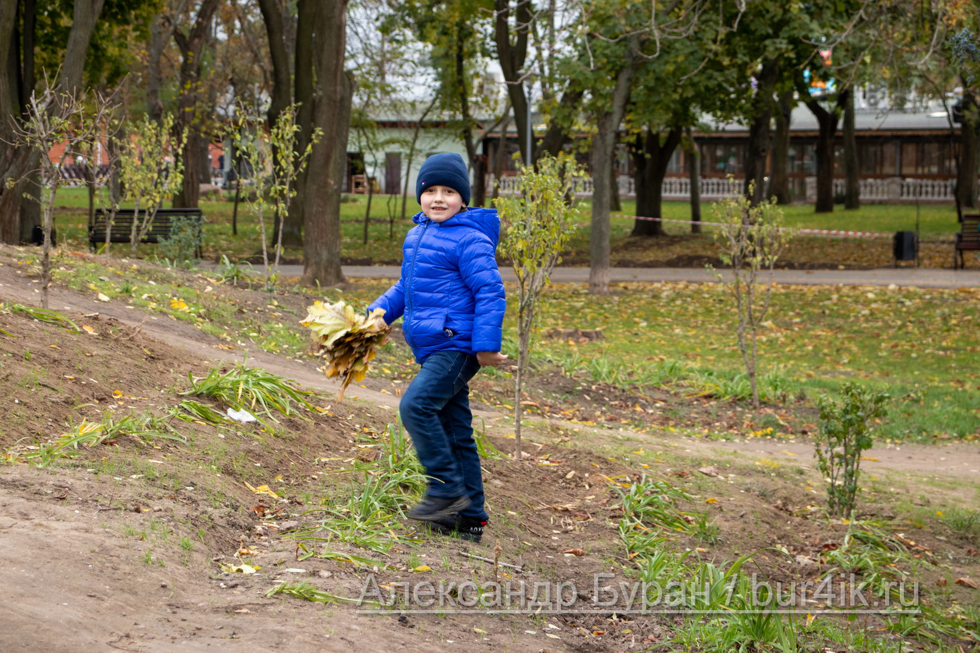 Мальчик в синей куртке поднимается на холм в осеннем парке