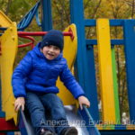 Мальчик в синей куртке катается на детской горкой в осеннем парке