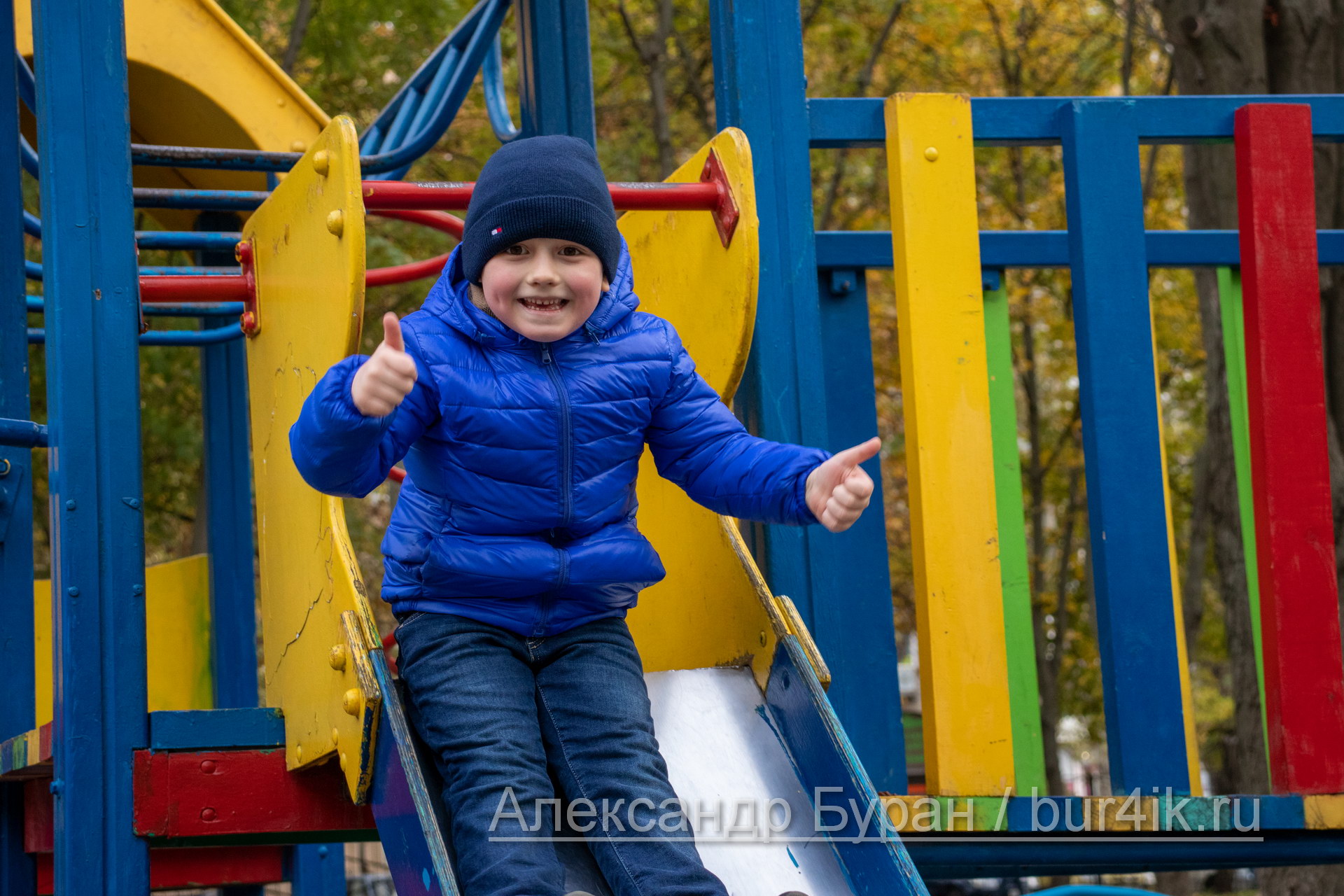 Мальчик едет вниз по склону холма в парке осенью