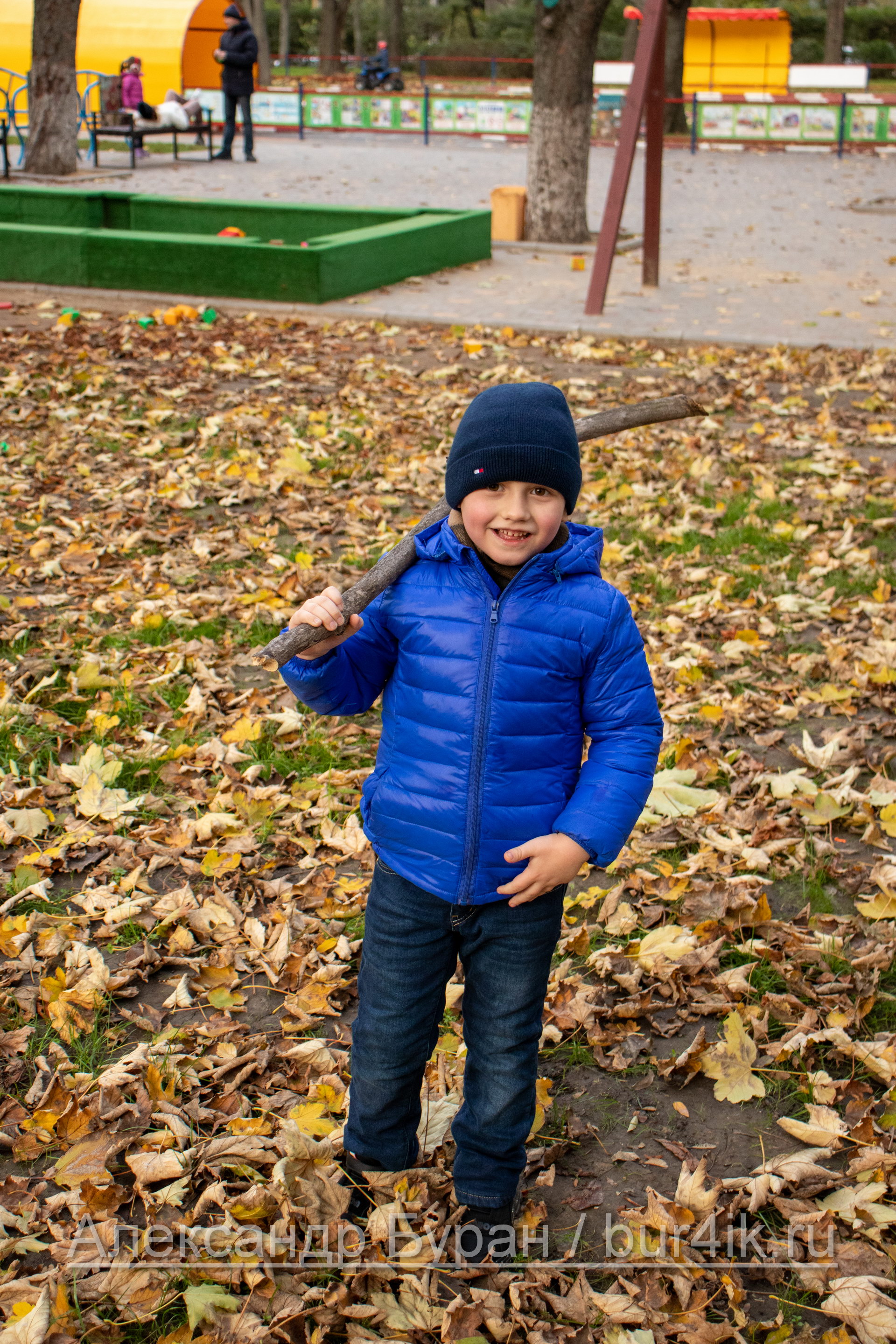 Мальчик в осеннем парке играет с сухой палкой из дерева