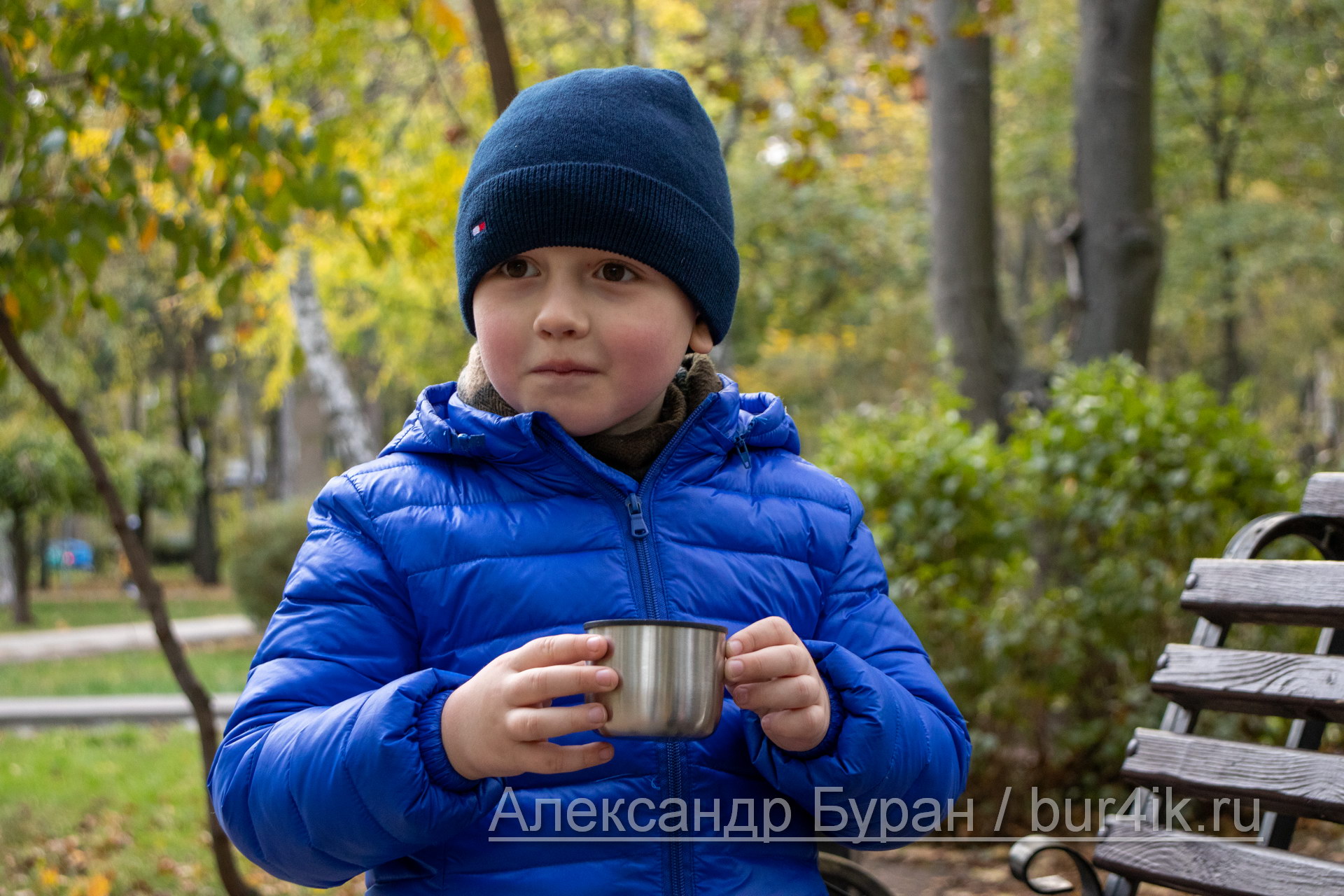 Мальчик в парке осенью пьет чай из крышки термоса