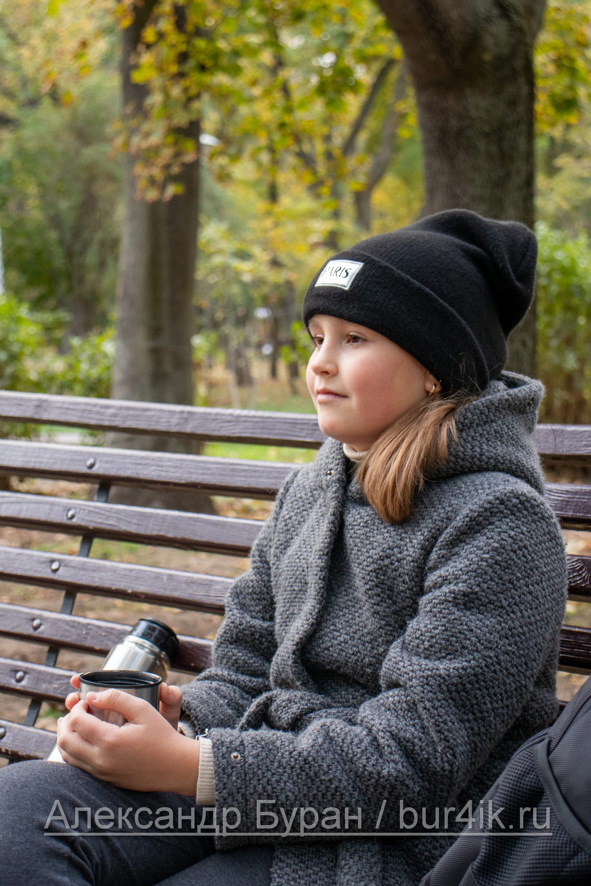 Девочка пьет теплый чай из термоса в парке осенью