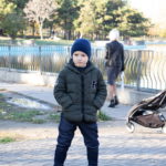 Шесть-летний мальчик стоит у пруда в осеннем парке