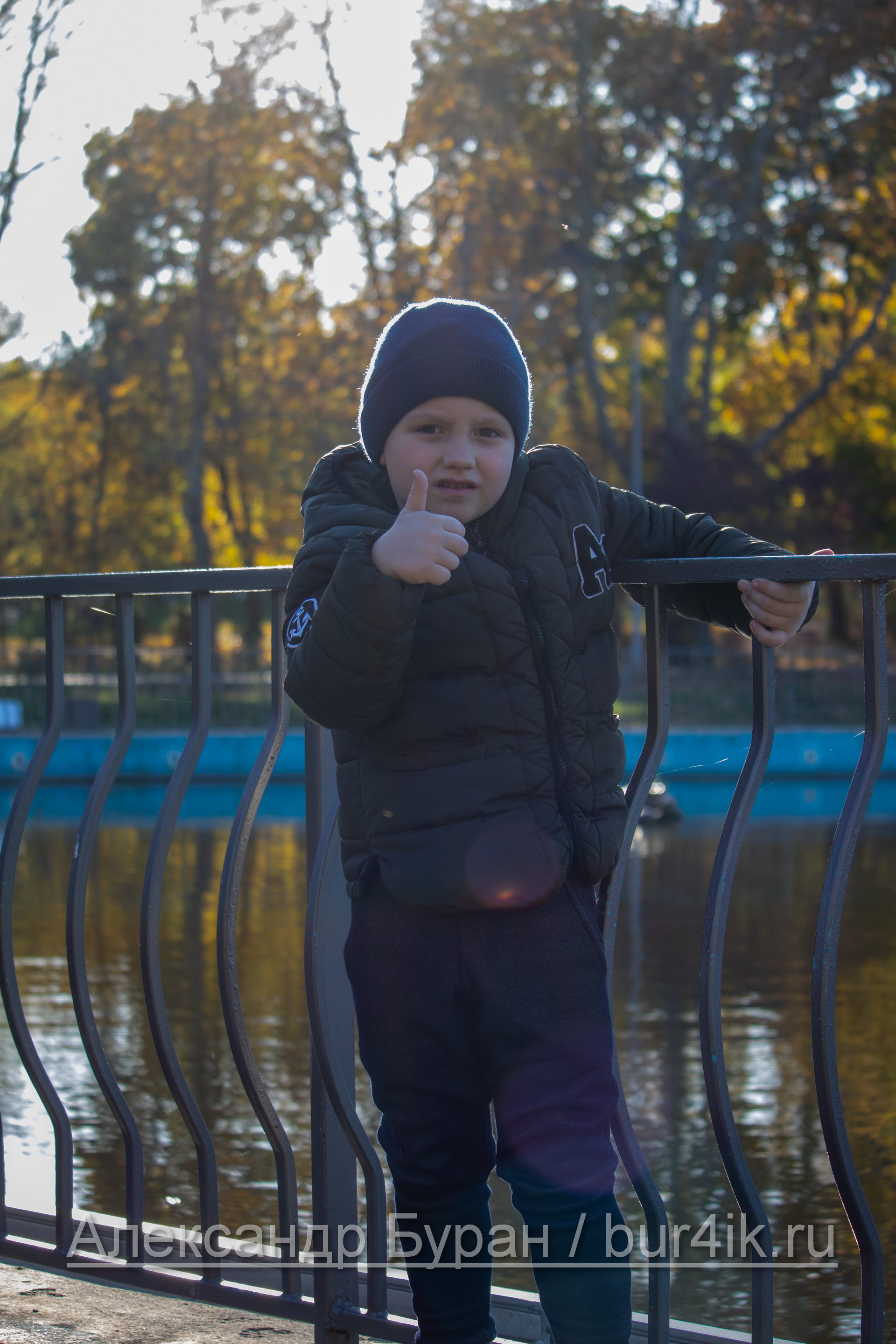 Мальчик на перила вокруг пруда в парке показывает большой палец