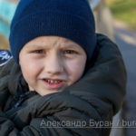 Мальчик в синей фуражке смотрит в камеру на прогулке в осеннем парке у пруда