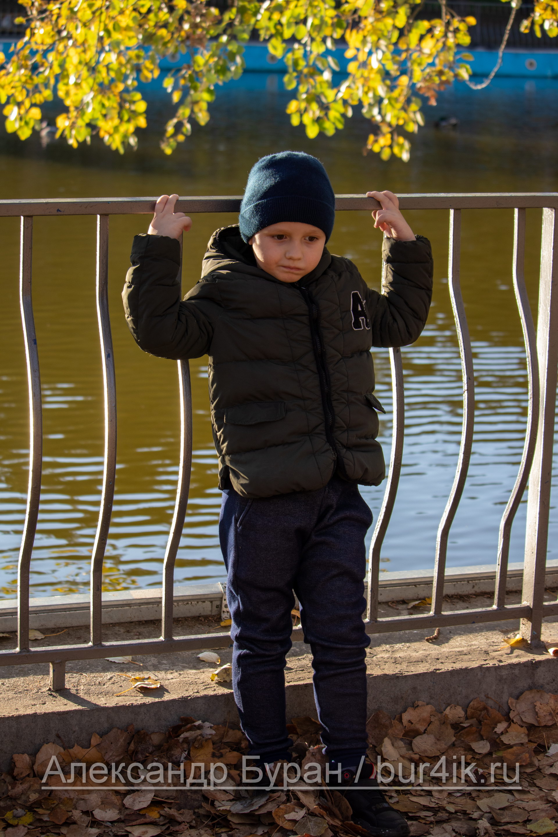 Мальчик спиной к озеру в парке и листва над головой
