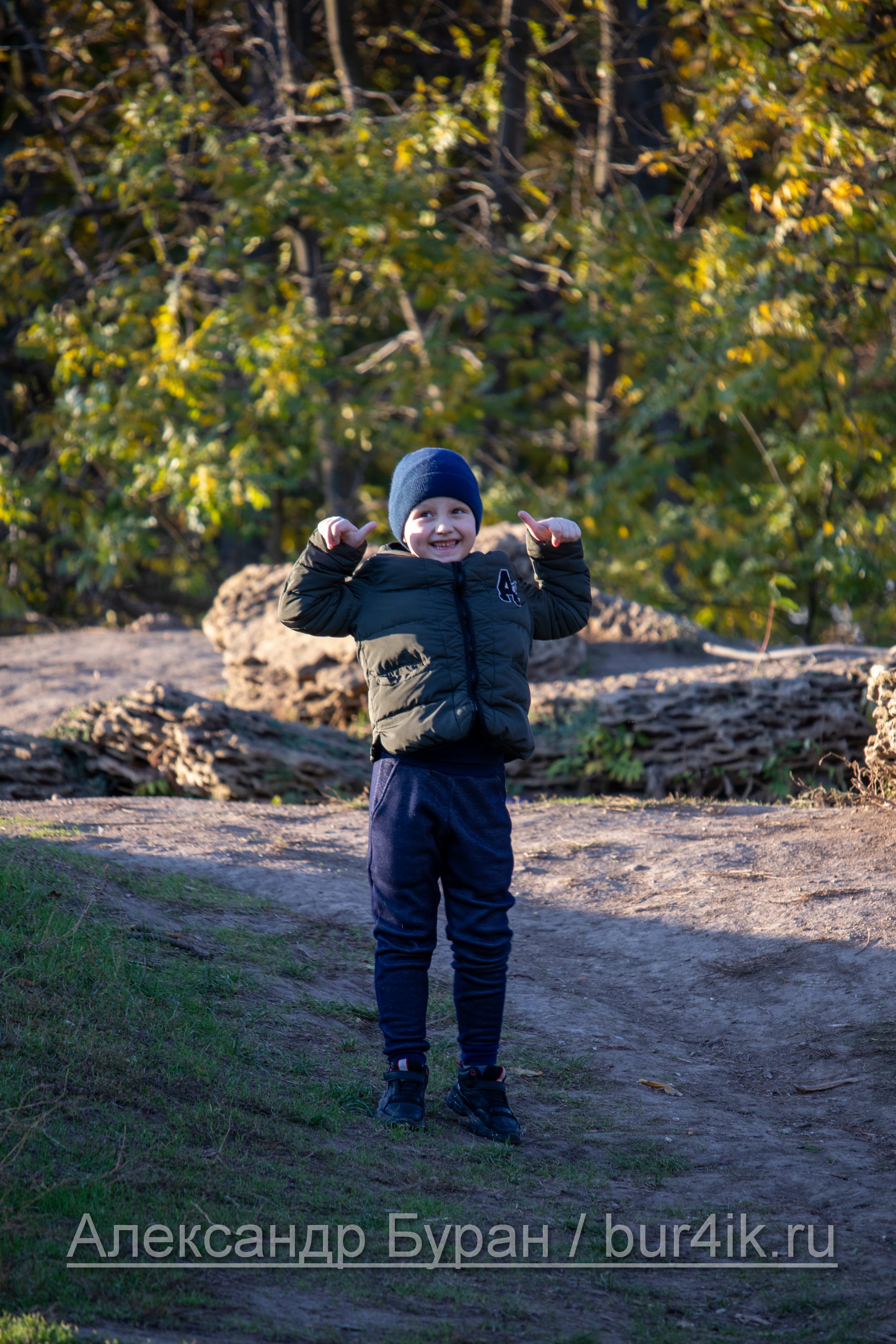 Мальчик в спортивных штанах и куртке на горе в парке