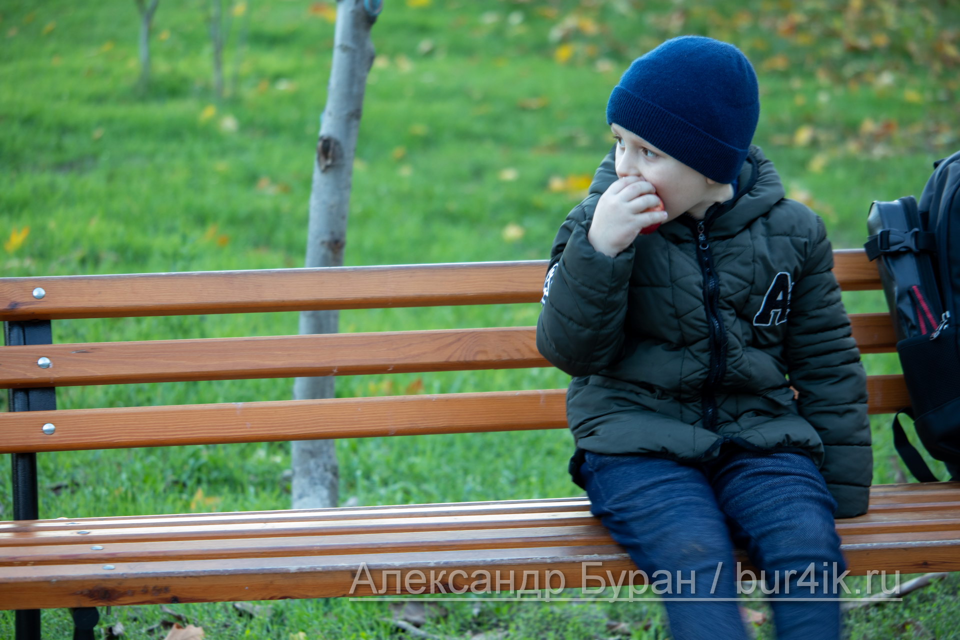 Мальчик ест яблоко на скамейке в осеннем парке