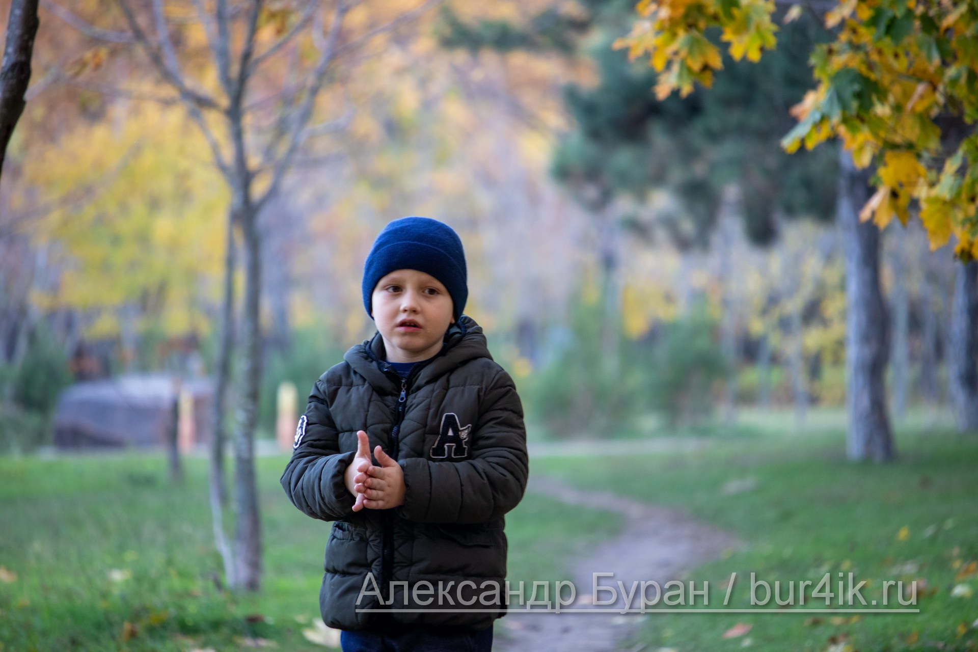Мальчик потирает руки, стоя на тропинке в осеннем парке