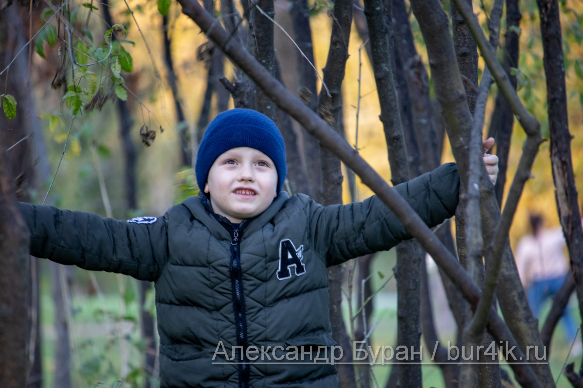 Мальчик среди ветвей молодых деревьев в парке осенью