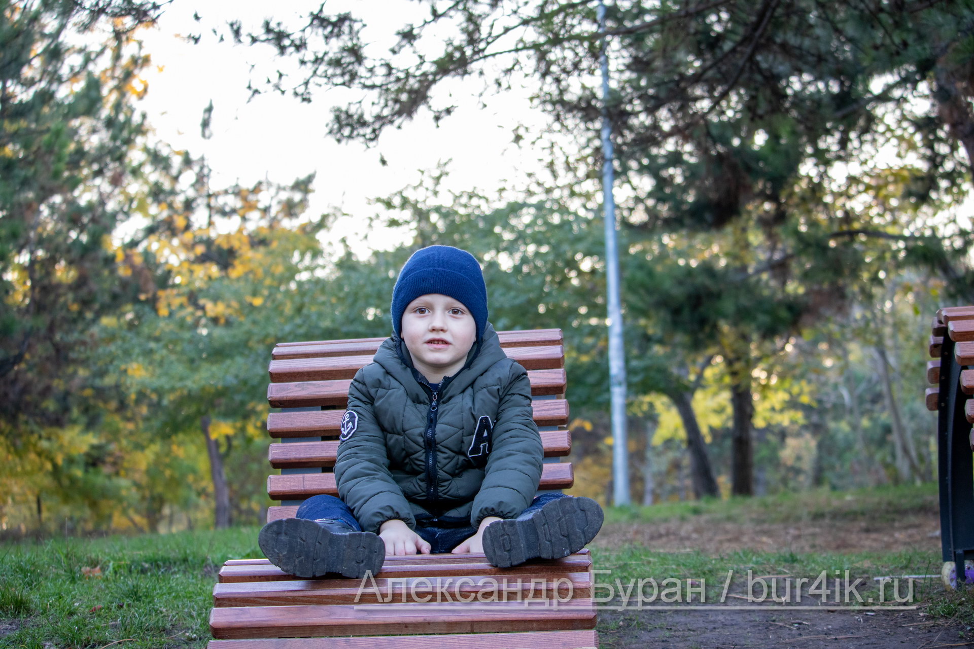 Мальчик сидит на деревянном топает осенью в парке