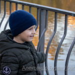 Мальчик стоит возле металлических перил, ограждающих озере в парке