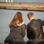 Парень и девушка фотографируют себя на смартфон, сидя у воды в порту