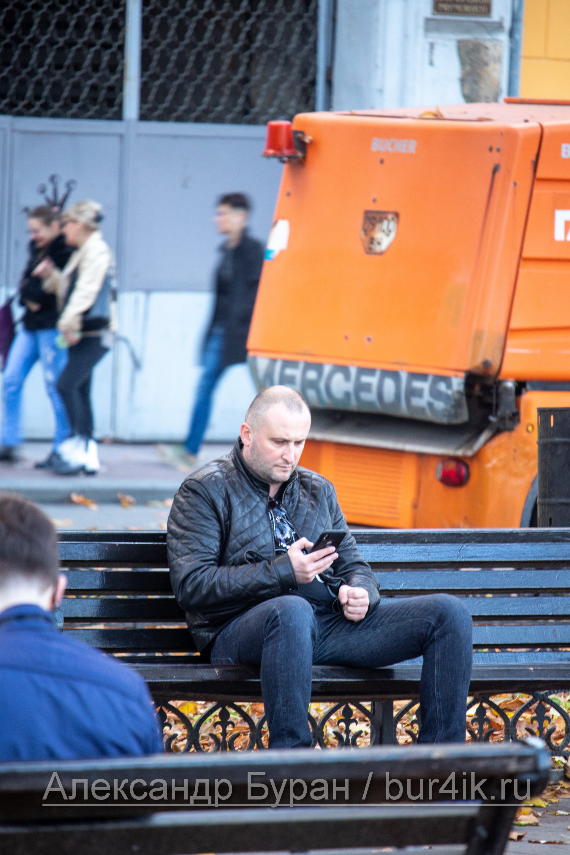 Мужчина средних лет сидит на скамейке в городском парке и смотрит на смартфон - Украина, Одесса, 09,11,2019