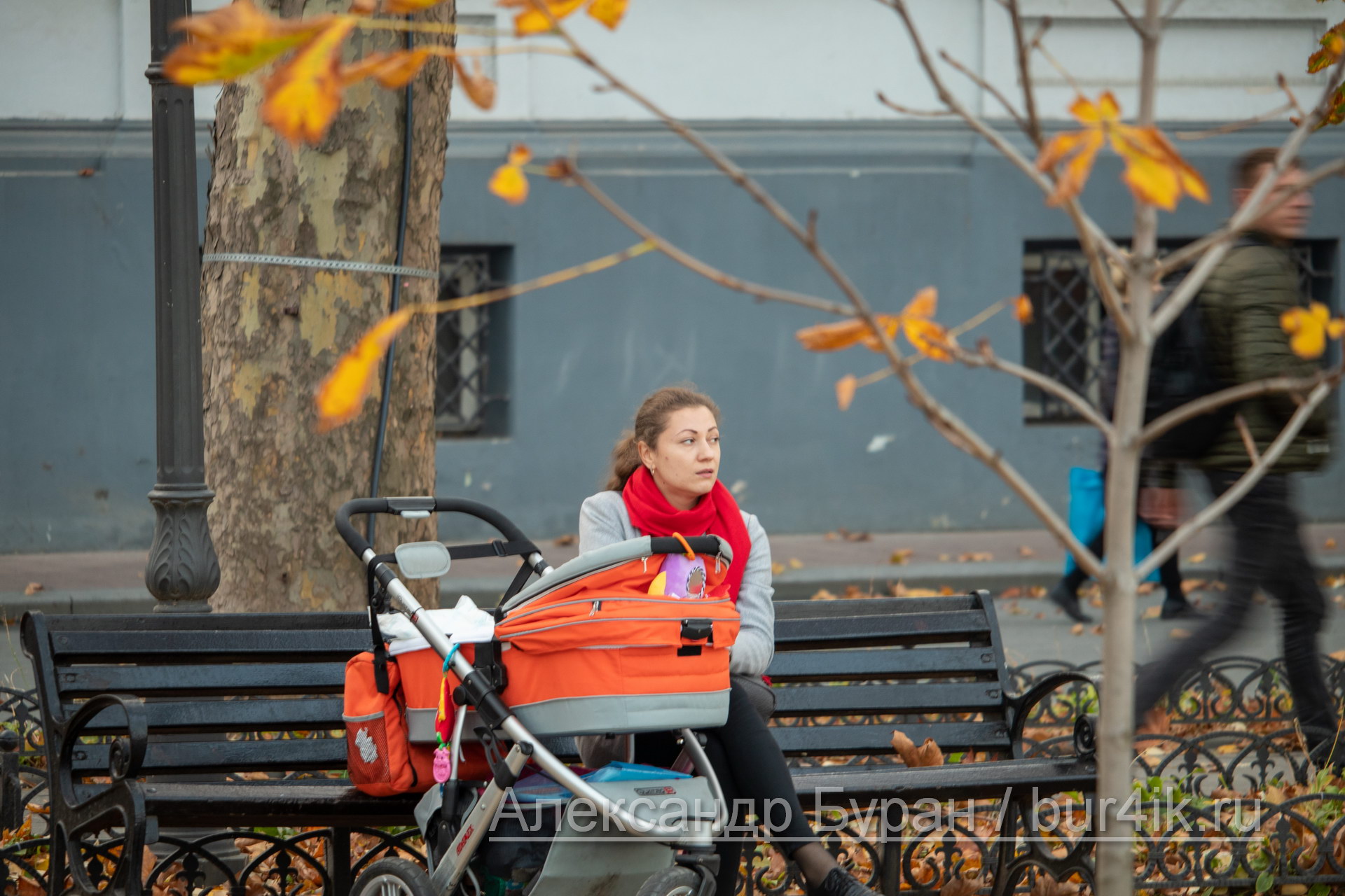 Женщина с оранжевым коляска и ребенок сидит на скамейке в парке - Украина, Одесса, 09,11,2019