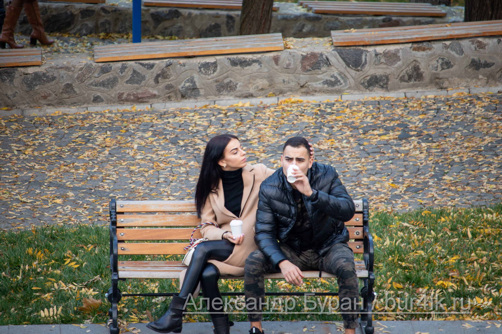 Девушка и парень пьют кофе из одноразовых стаканчиков на скамейке в парке осенью - Украина, Одесса, 09,11,2019