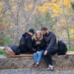 Два парня и одна девушка сидят в парке на скамейке и смотреть что-то в телефоне, осенью - Украина, Одесса, 09,11,2019
