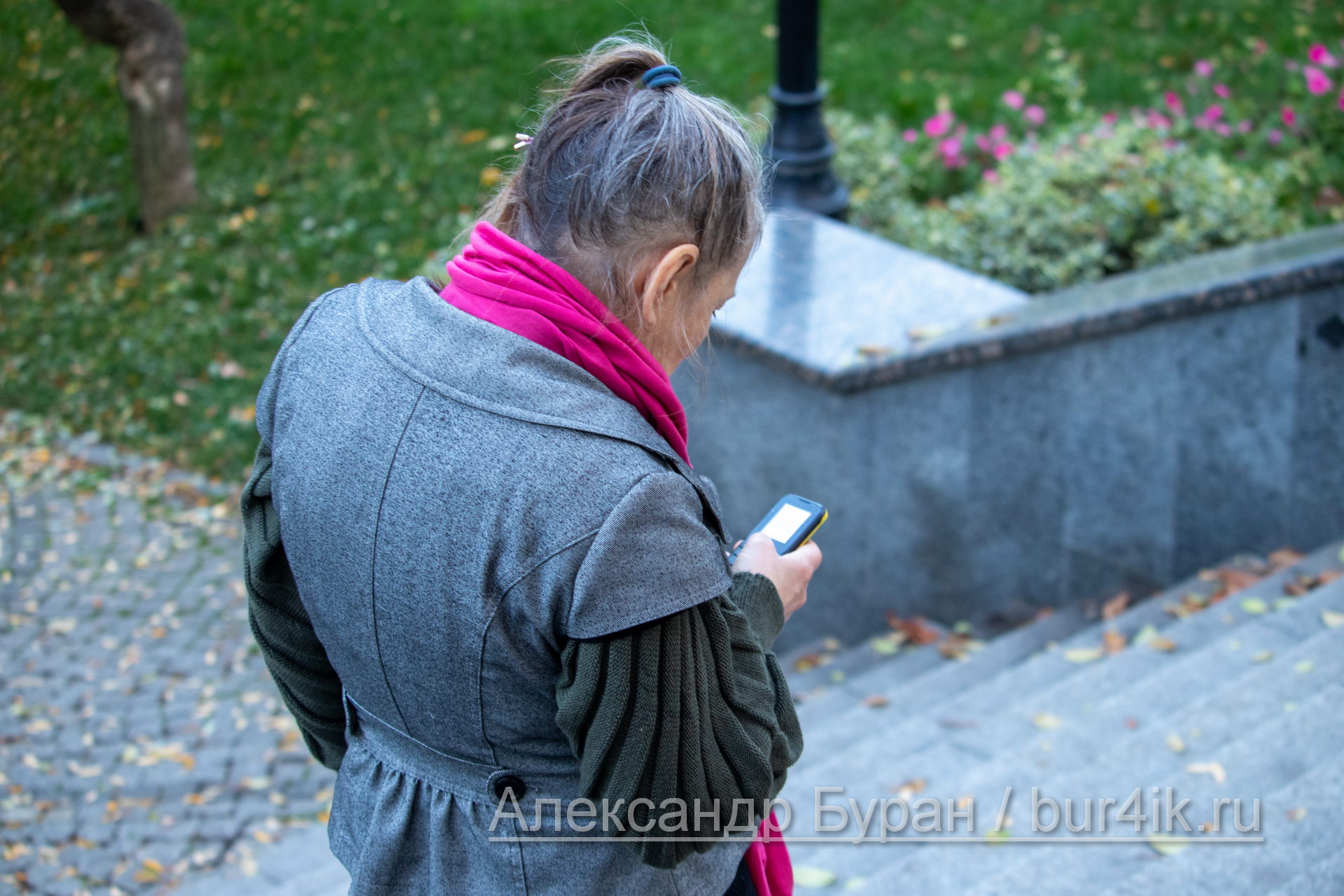 Седая женщина в возрасте смотрит на старого телефона на улице осенью