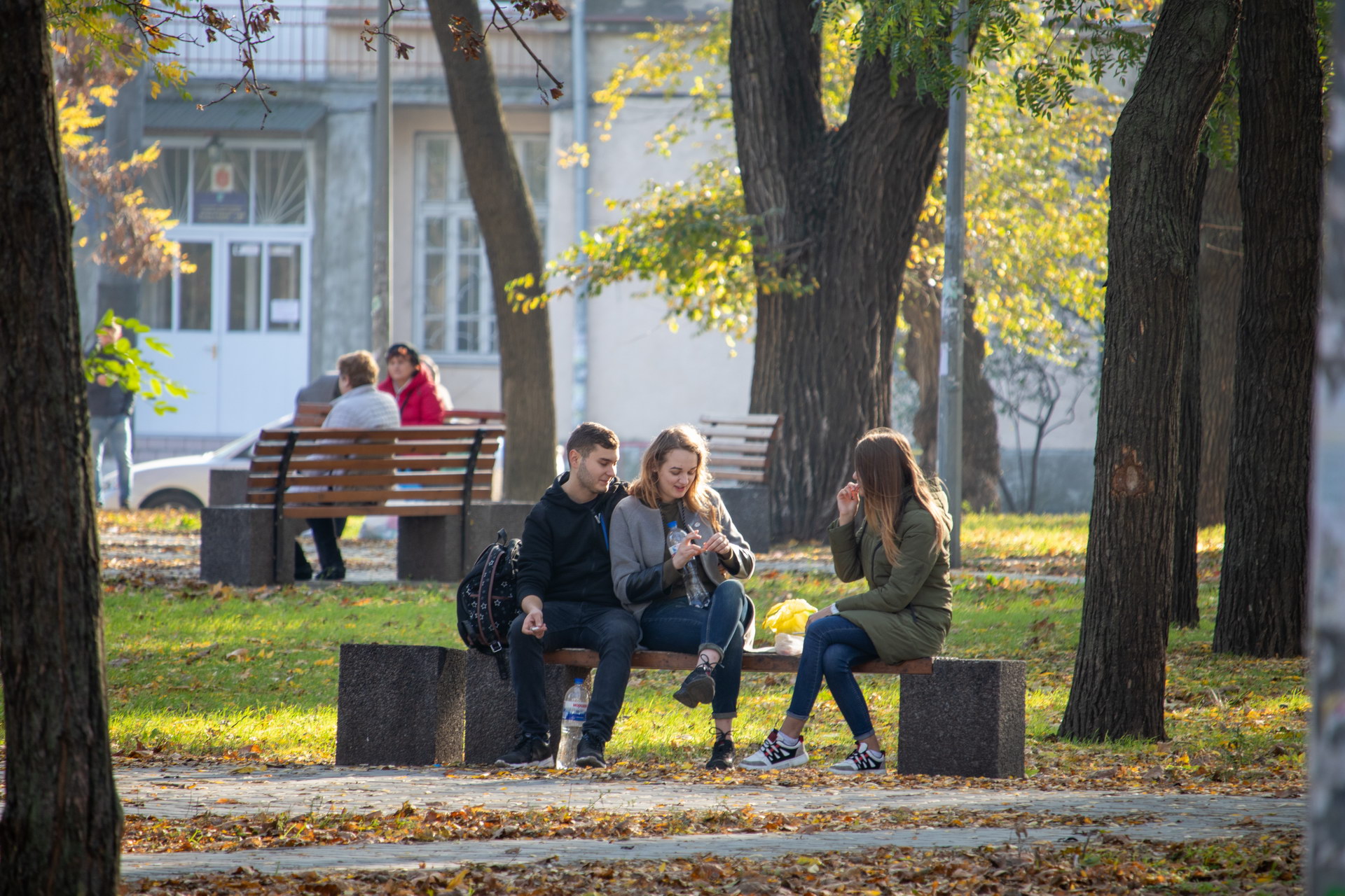 Две девушки и парень сидят на скамейке в парке осенью – bur4ik.ru фото 1