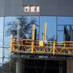 Мужчина моет стеклянный фасад здания на желтой подвесной люльке – bur4ik.ru фото 1