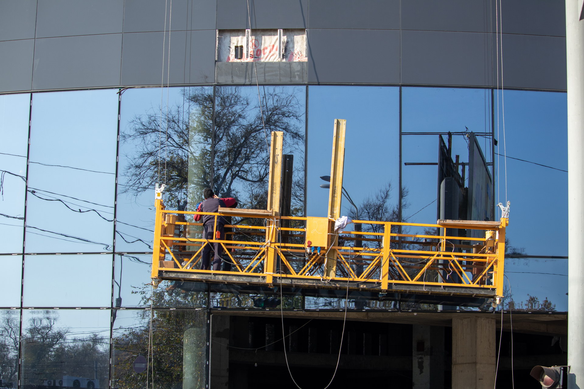 Мужчина моет стеклянный фасад здания на желтой подвесной люльке – bur4ik.ru фото 1