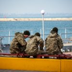 Военные сидят на скамейке у причала в порту в городе Одесса