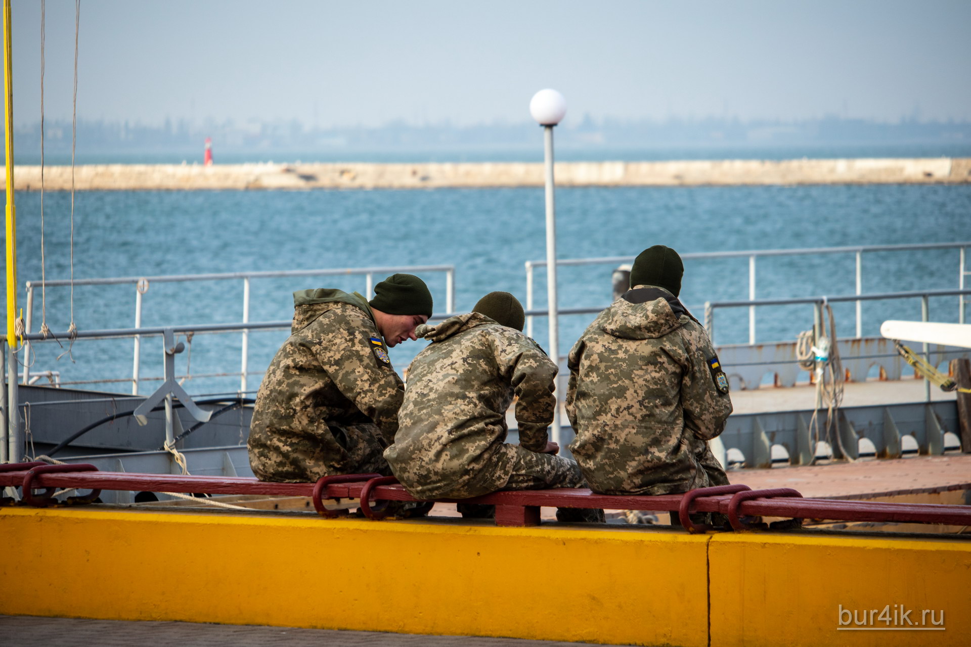 Военные сидят на скамейке у причала в порту в городе Одесса