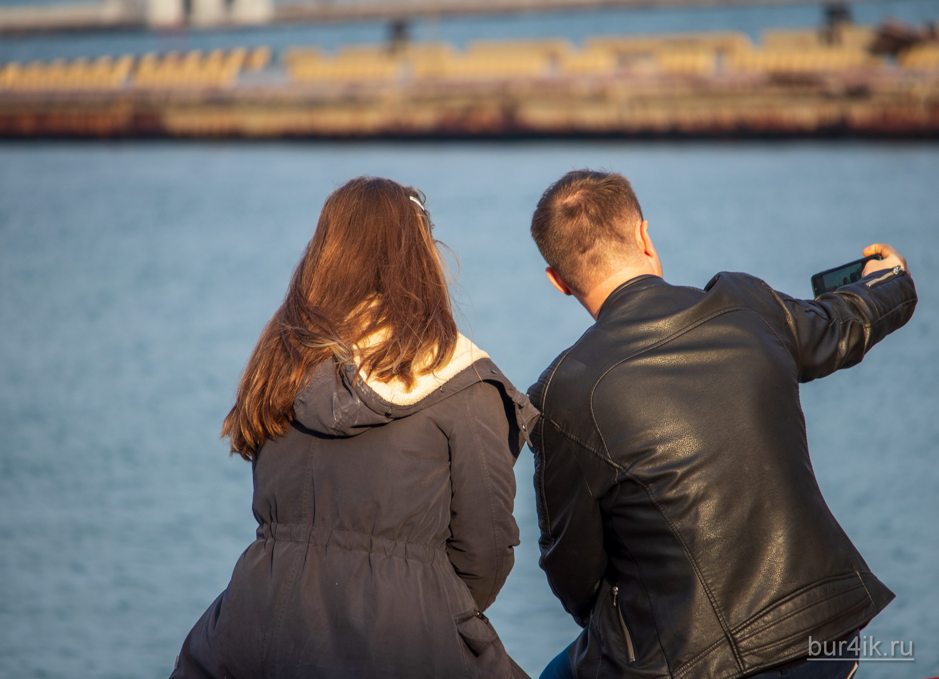 Парень и девушка сидя на скамейке делают серфи в порту города Одесса 2