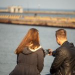 Парень и девушка сидя на скамейке делают серфи в порту города Одесса 3