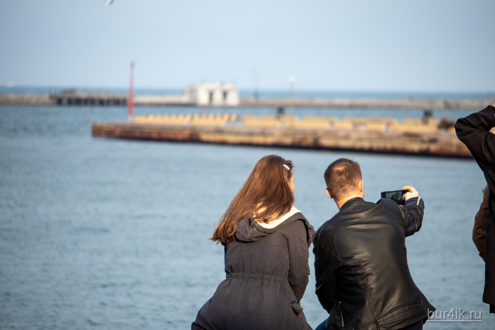 Парень и девушка сидя на скамейке делают серфи в порту города Одесса
