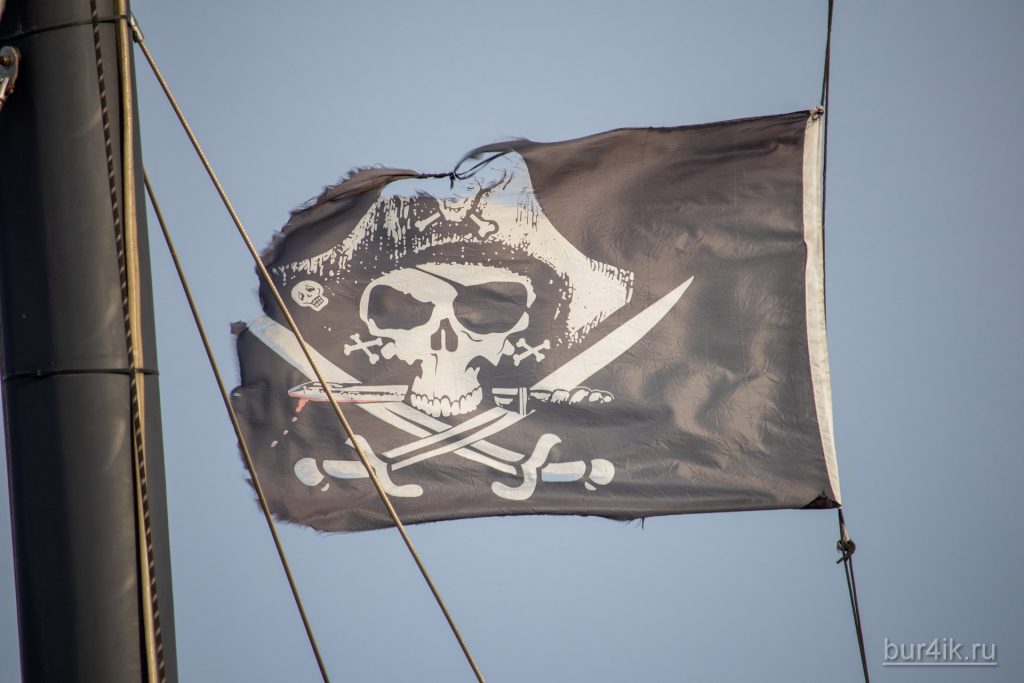 Черный пиратский флаг с черепом и саблями на мачте фрегата
