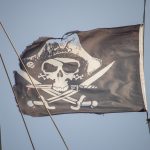 Черный пиратский флаг с черепом и саблями на мачте фрегата