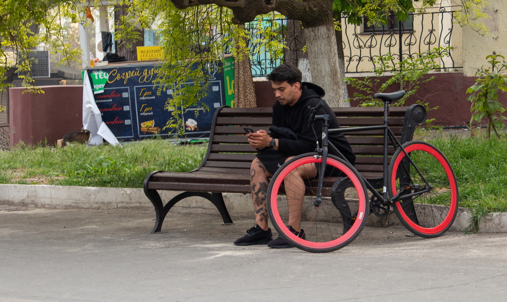 A cyclist with a phone in his hands sits on a bench - Ukraine, Odessa, 11,06,2020