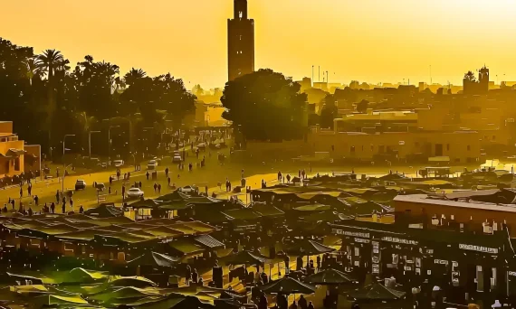 Фотография площади Джемаа-эль-Фна в Марокко, залитой теплым закатным светом. Оживленная сцена с торговцами, людьми и минаретом мечети Кутубия.